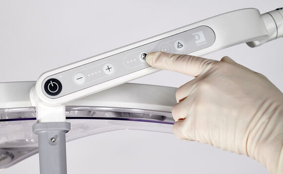 Hand mit Handschuh bedient das Touchpanel einer OP-Leuchte zur Einstellung von Licht und Position